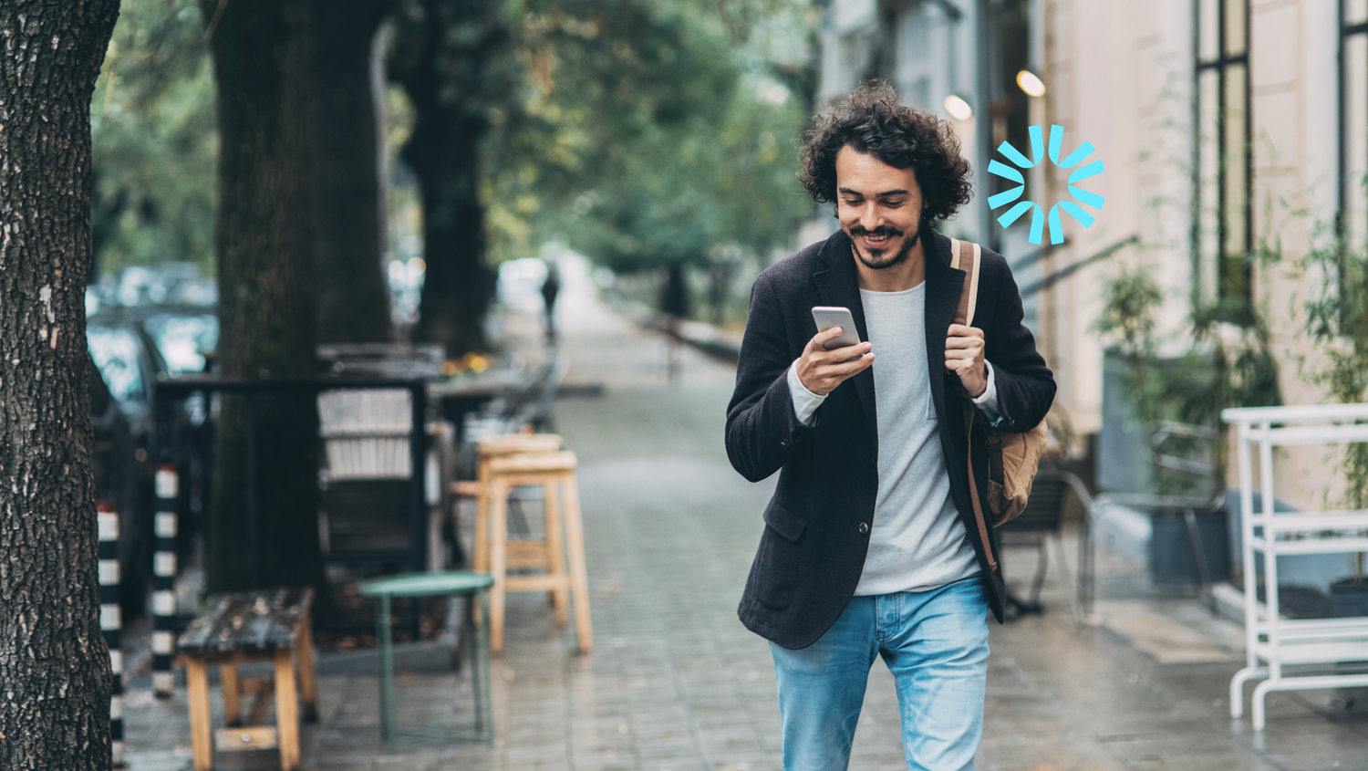 A man smiles while looking at his phone walking down the street.