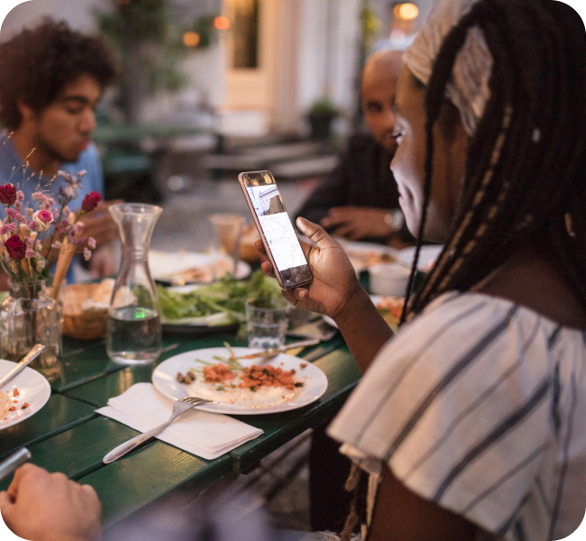 A woman looking at her phone while having dinner with friends at a backyard dinner party.