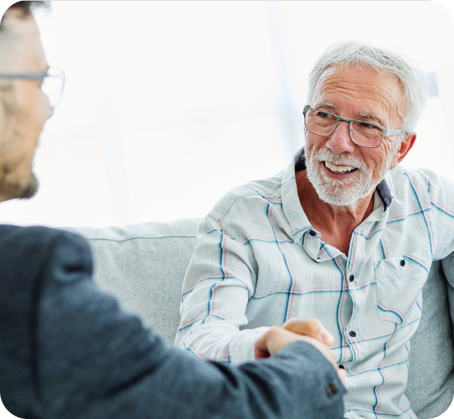 An older man with glasses shakes hand with a younger man in an office setting