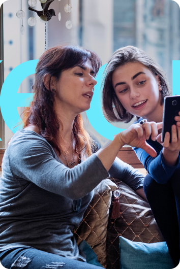 A picture of two women, with one woman pointing something out on her friend’s phone.