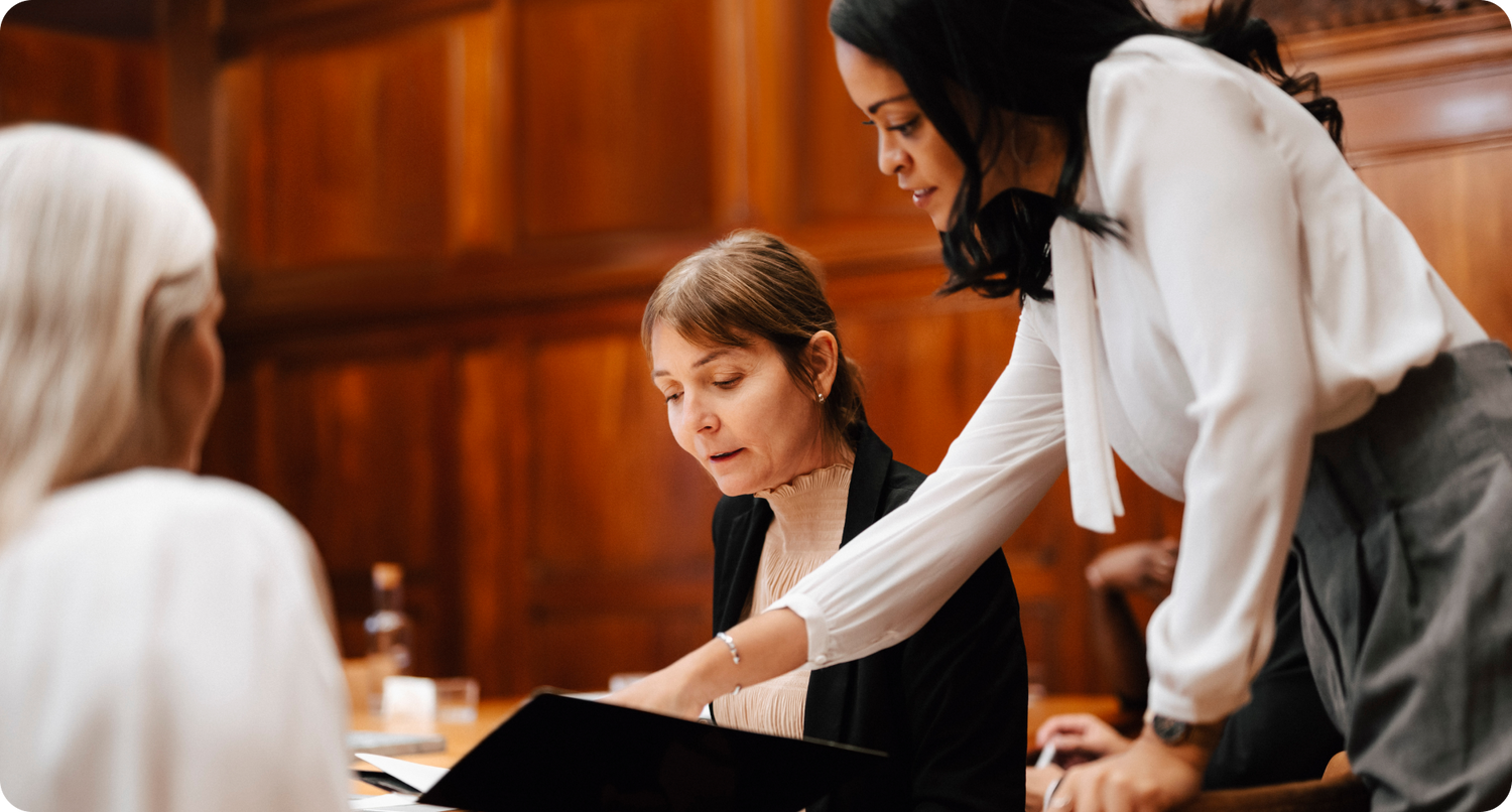 two professionally dressed women reviewing notes in a courtroom setting