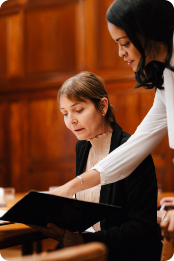 two professionally dressed women reviewing notes in a courtroom setting