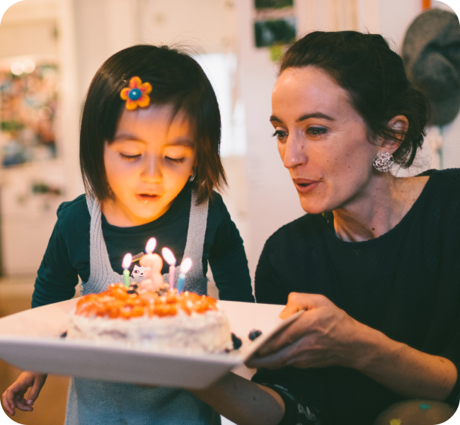 A mother holds a birthday cake while her young child is about to blow out the candles. 