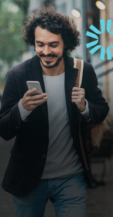 A man smiles while looking at his phone walking down the street.