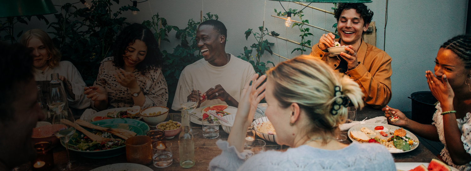 A lively multicultural group of friends sharing a laugh during a backyard dinner party. 