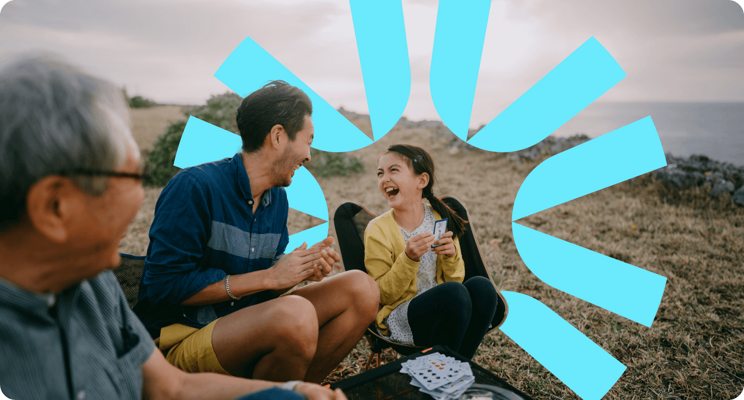 A multi generational family share a laugh as they play cards and enjoy the sunset together.