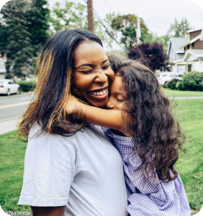 A mother and daughter share a laugh and warm embrace on the front lawn.