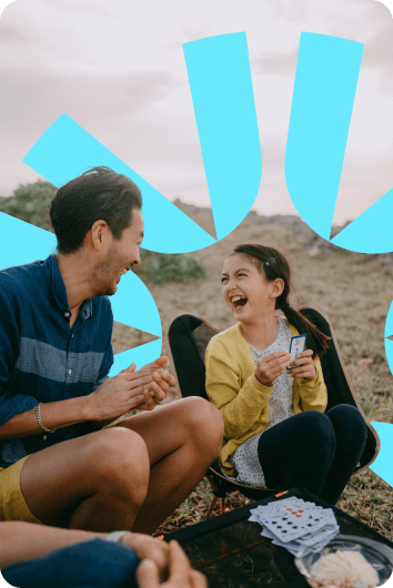 A multi generational family share a laugh as they play cards and enjoy the sunset together.