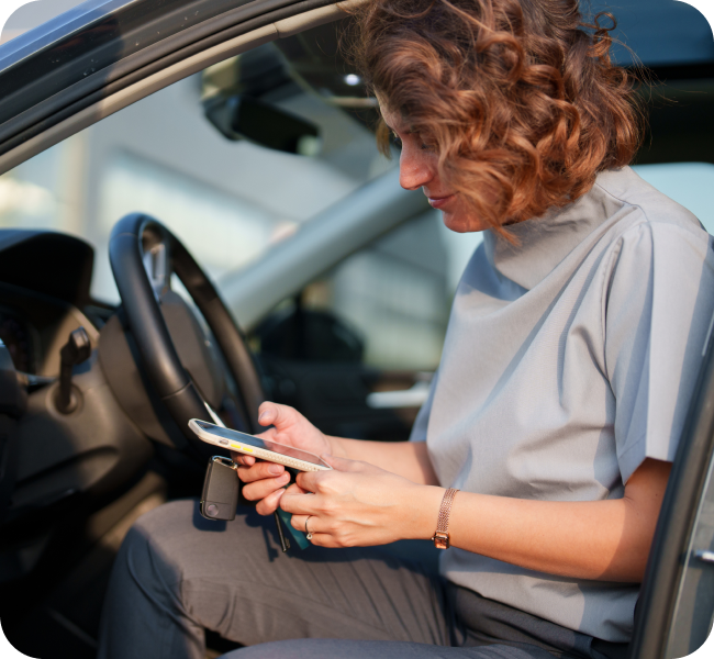 a woman looks at her phone in her car.